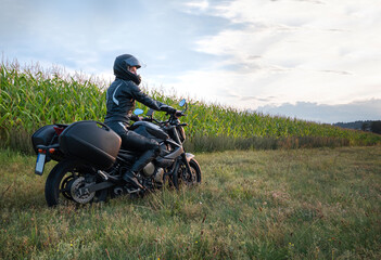 sense of adventure she and her motorcycle resting for a moment on the side of a rural road of sun-drenched agricultural fields in the golden hour