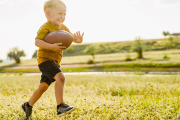 Blonde white boy smiling while playing with rugby ball