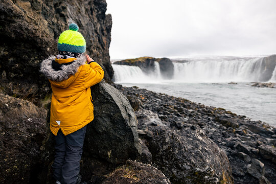 Young Boy in Yellow Jacket taking a picture at Goðafoss Waterfall Iceland