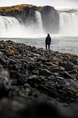 Obraz premium Goðafoss Waterfall Iceland Woman Black Jacket standing lonely in front of the waterfall