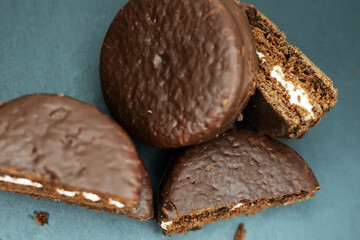 Cookies in chocolate glaze and white cream filling scattered on a dark background. Top view.