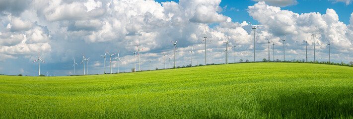 Panoramic view over beautiful farm landscape with wheat field as a wave and wind turbines to...