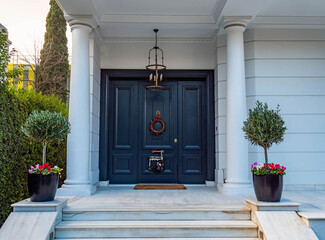 Christmas wreath decorated house entrance dark green door, with potted flowers and marble stairs.