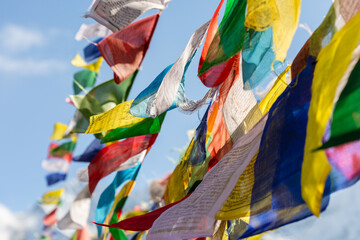 Long strings of Tibetan prayer flags flutter in the wind against blue sky high in the mountains.