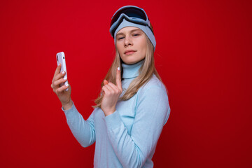 Portrait of a young woman in a sweater and ski goggles with a phone