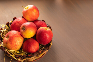 A vase of red apples on a uniform brown background. Wicker basket with harvest fruits