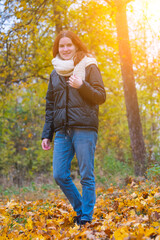 a portrait of a red - haired smiling girl in a jacket and scarf with her hair loose in full growth walks in the park . against the background of autumn nature, the concept of human emotion