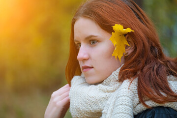 portrait of a red - haired smiling girl in a jacket and scarf with her hair down and maple leaves behind her ear . against the background of autumn nature, the concept of human emotion