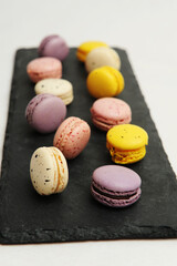 Colorful french macarons on black slate board, white background