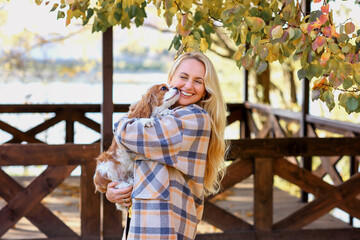 girl in a plaid shirt in autumn in the park with a dog cavalier king charles spaniel