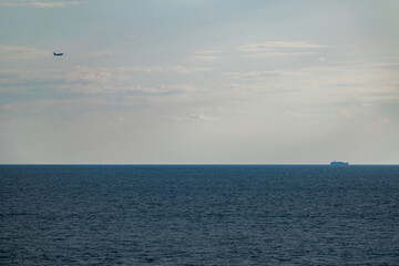 Airplane over the sea and blue sky with yellow clouds and ship.