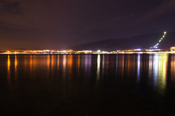 Fototapeta na wymiar Night city with lights and mountains by the sea and red sky.