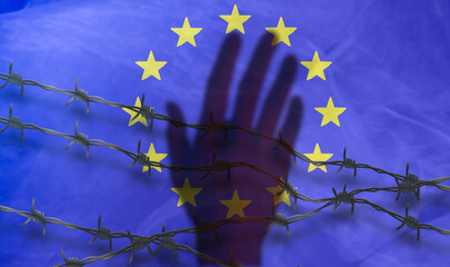 The shadow of the hand behind the barbed wire on the background of the EU flag.Metal fence with...