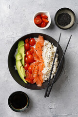 Poke bowl - black bowl with white rice, smoked salmon, cherry tomatoes and avocado, sesame seeds,...
