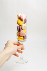 Mini colorful french macarons in a champagne glass in hand, white background. Holiday aesthetic