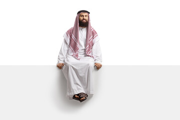 Saudi arab man sitting on a blank panel and looking at camera - obrazy, fototapety, plakaty