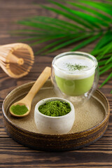 Matcha tea powder with whisk and palm branch on a wooden table.