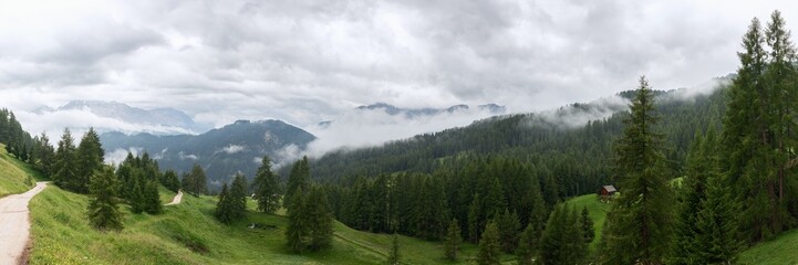 A panorama of the Italian Dolomites covered with fog and a hiking trail through the forest