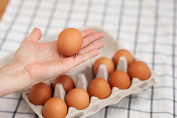 Chicken brown eggs are in a cardboard box bought at a grocery store. Healthy breakfast. A tray for carrying and storing fragile eggs. Woman takes one egg out of the package with her hand