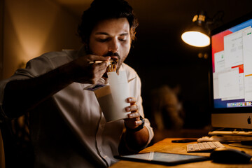 White man eating asian noodles while working with computer