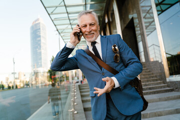 Senior man talking on cellphone while standing by building