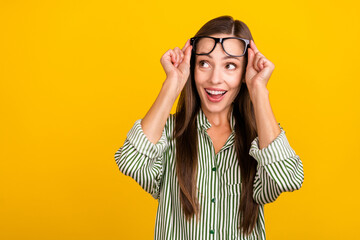 Photo of young cheerful excited woman hands touch eyeglasses look empty space curious isolated over yellow color background