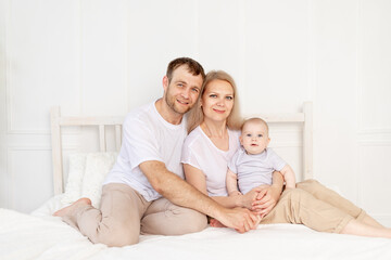 Obraz premium happy family mom, dad and baby play on the bed at home and have fun