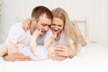 Obraz na płótnie Canvas happy family mom, dad and baby play on the bed at home and have fun