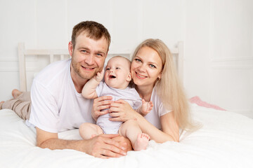 Fototapeta na wymiar happy family mom, dad and baby play on the bed at home and have fun