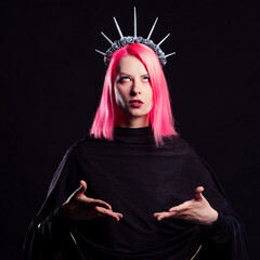 A gothic diva with pink hair in a royal image, a crown with roses and rays on her head, open arms stretched out to you