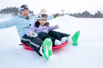 young father and daughter play on sledge in ski resort