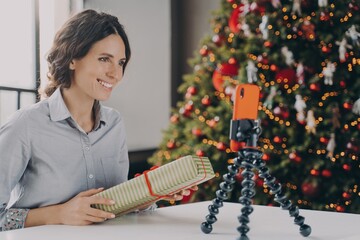 Smiling positive female blogger recording video tutorial about tips for wrapping Christmas presents