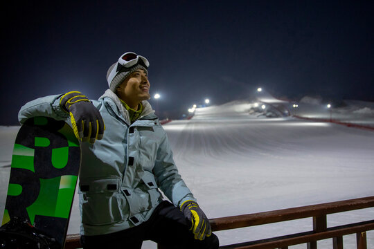 Young Man Sitting On The Fence Watching Far Away In Ski Resort
