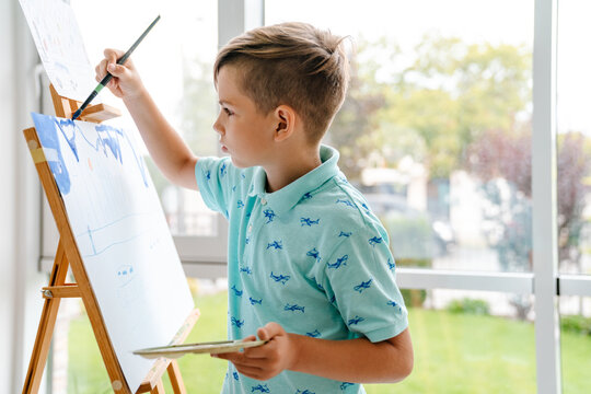 White Blonde Boy Drawing During Class In Art School Indoors