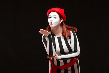 Portrait of female mime artist performing, isolated on black background. Woman blows a kiss posing...
