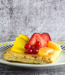 Fruit tartlet, red currants, mango, tangerine, presented on porcelain plate. Stone background and copy space.