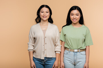 cheerful asian mother and adult daughter looking at camera isolated on beige