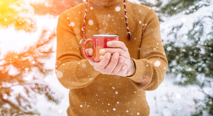 Mulled wine or tea and cocoa in the hands of a men during a snowfall in the forest. Winter hot...