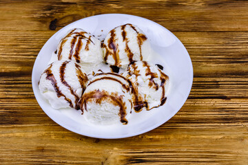 Plate with ice cream balls and chocolate topping on a wooden table