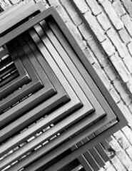 Geometric abstraction from several metal straight rods against the background of a brick wall. Black and white photo