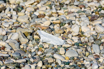 A disposable face mask discarded on pebble at the beach