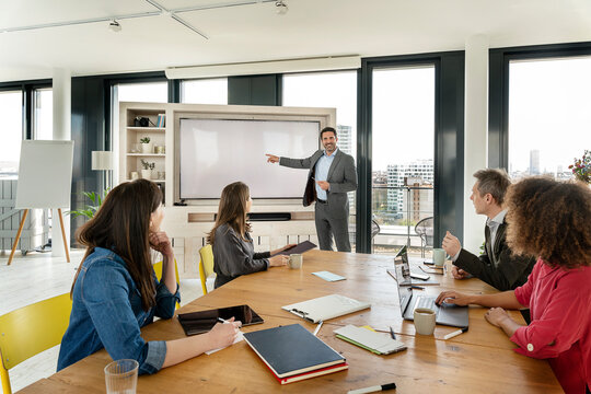 Smiling male professional explaining on projection screen to colleagues during meeting at office