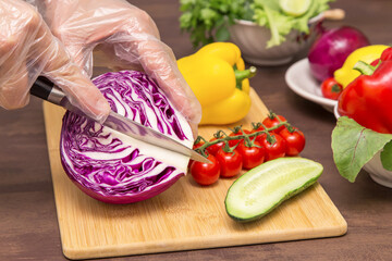 Different vegetables for cooking healthy vegetarian vegan diet food. Chef hands in cellophane gloves cutting violet cabbage close up