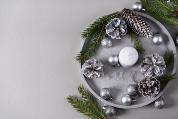 Concrete tray with a candle, pine cones, fir branches, silver Christmas balls on a gray background...