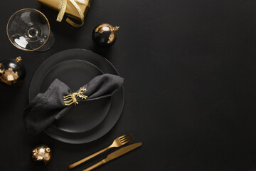 Christmas table setting with black plates, gold deer ring, gift and gold cutlery. Golden gilded...