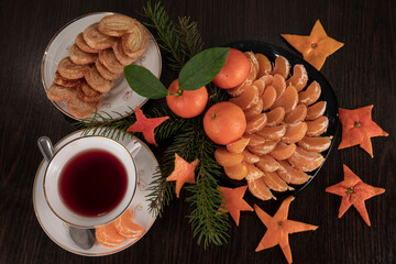 Top view of tangerines with leaves in Christmas decor with Christmas tree, dried orange and berries over old wooden table. Dark rustic style