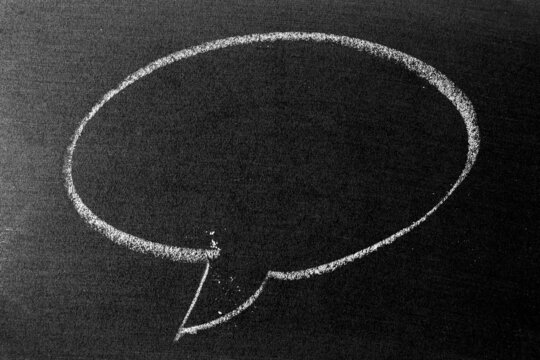 White color chalk hand drawing in round bubble speech shape with blank space on blackboard or chalkboard background