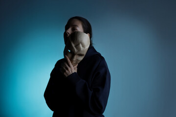 Hiding behind a mask, a young woman in a dark hoodie hides her face with a mask,...