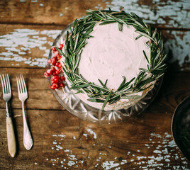 In focus cake with white cream, decorated red berries and rosemary.