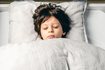 European cute little boy sleeping in the bed at home